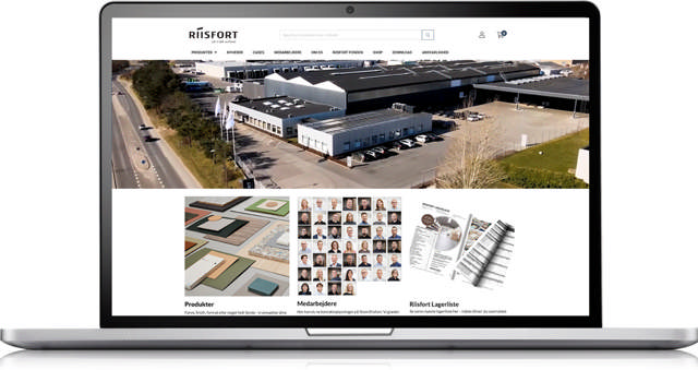 En bærbar computer viser en hjemmeside med et luftfoto af en stor industribygning. Nedenunder er der sektioner for produkter, medarbejderfotos og kataloger.